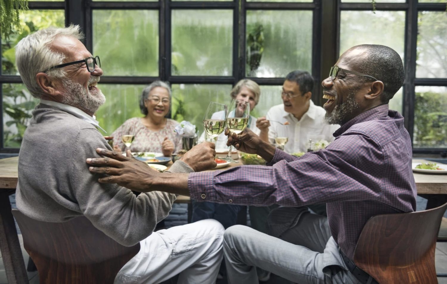 A group of elderly friends toasting a glass of wine as they gather for dinner in Cincinnati, OH.