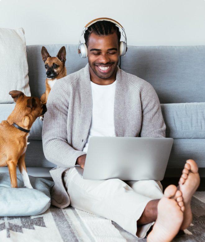 Man sitting on floor of home with headphones and laptop and two dogs in Cincinatti, Ohio
