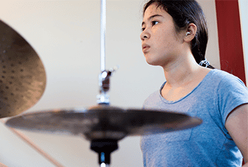A female drummer wearing hearing aids practicing in Cincinnati, OH.